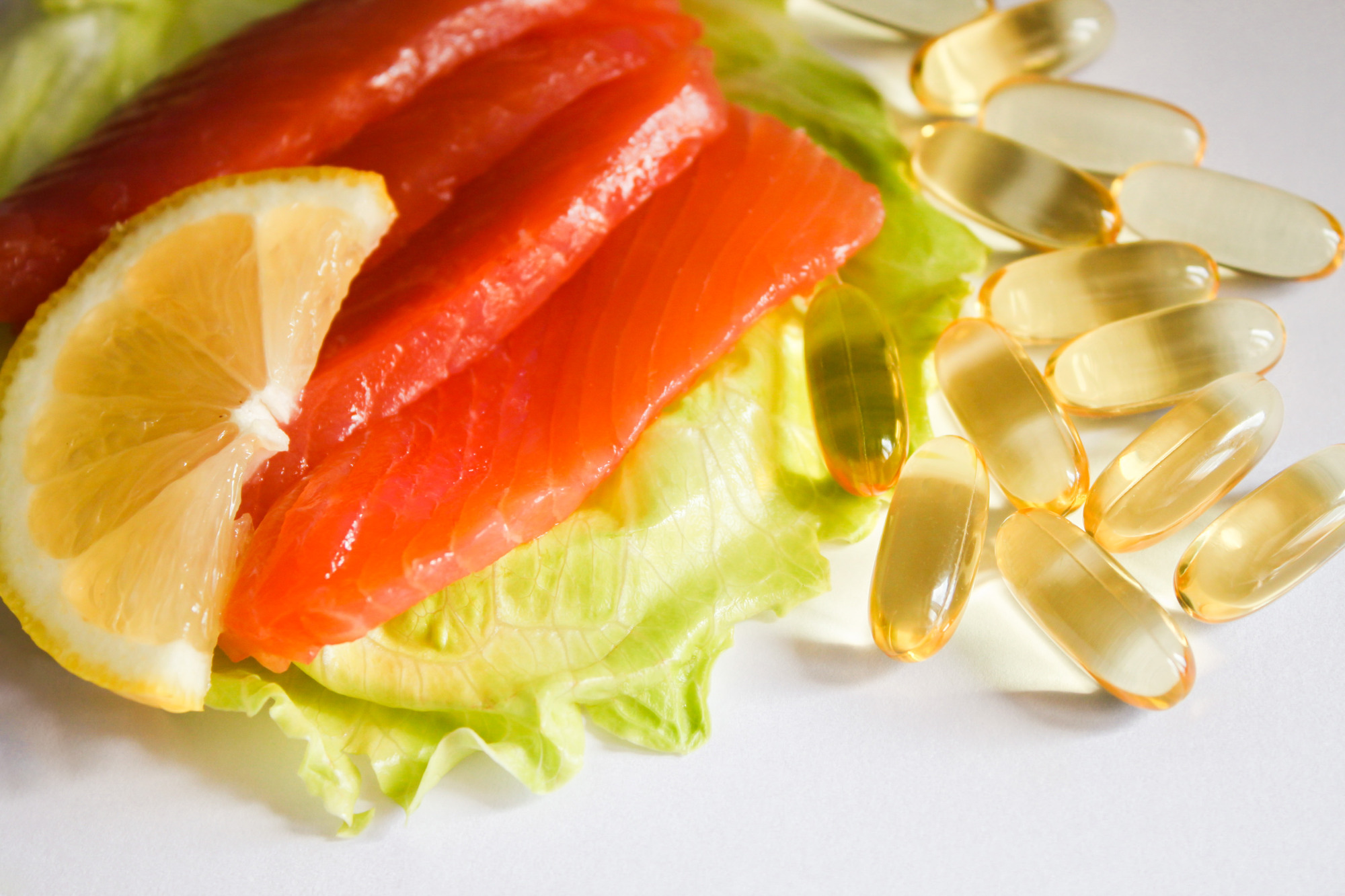 Omega-3 capsules, salmon, lemon on lettuce.