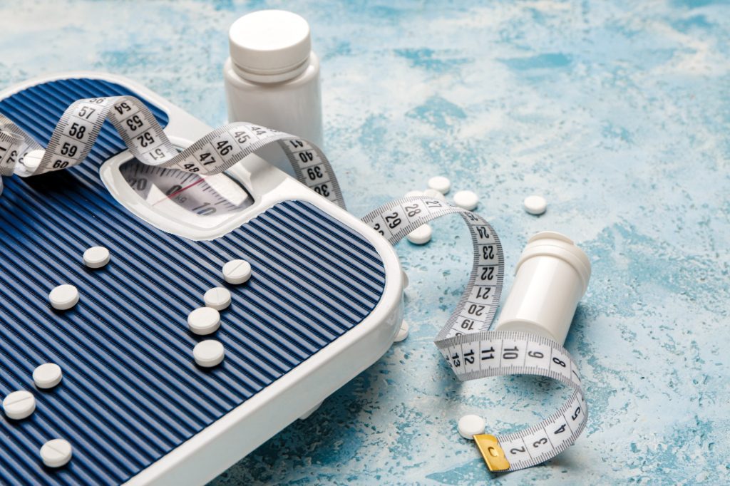 weight loss drugs on scales and measuring tape
