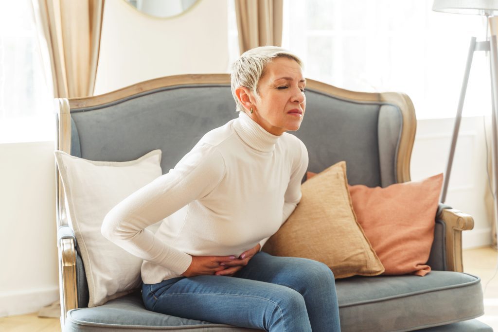 Senior woman on a couch clutching stomach in pain.