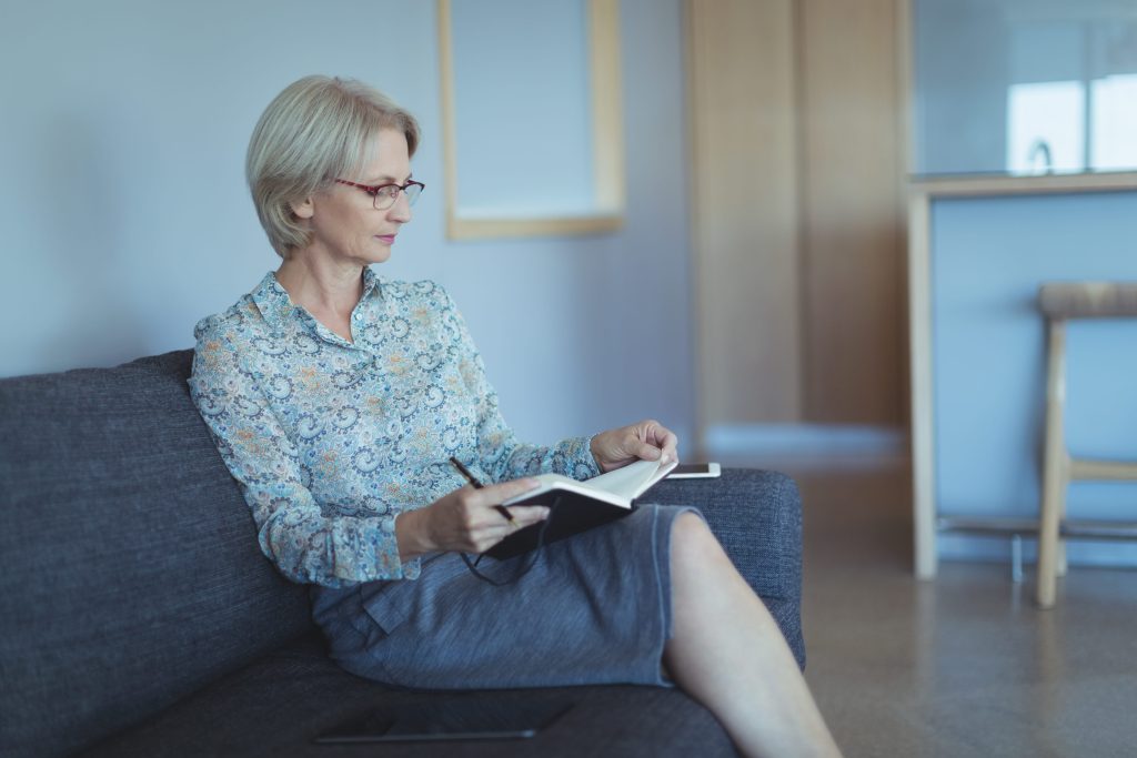 Woman sitting on couch writing on her journal notebook