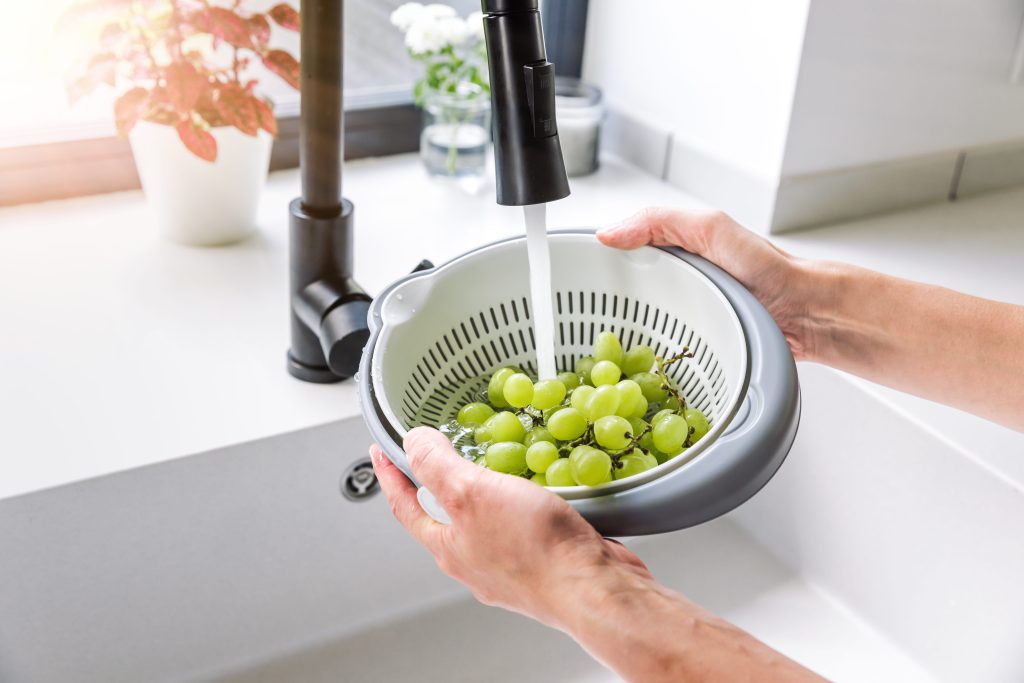 Green ripe grapes being washed with running water on a colander