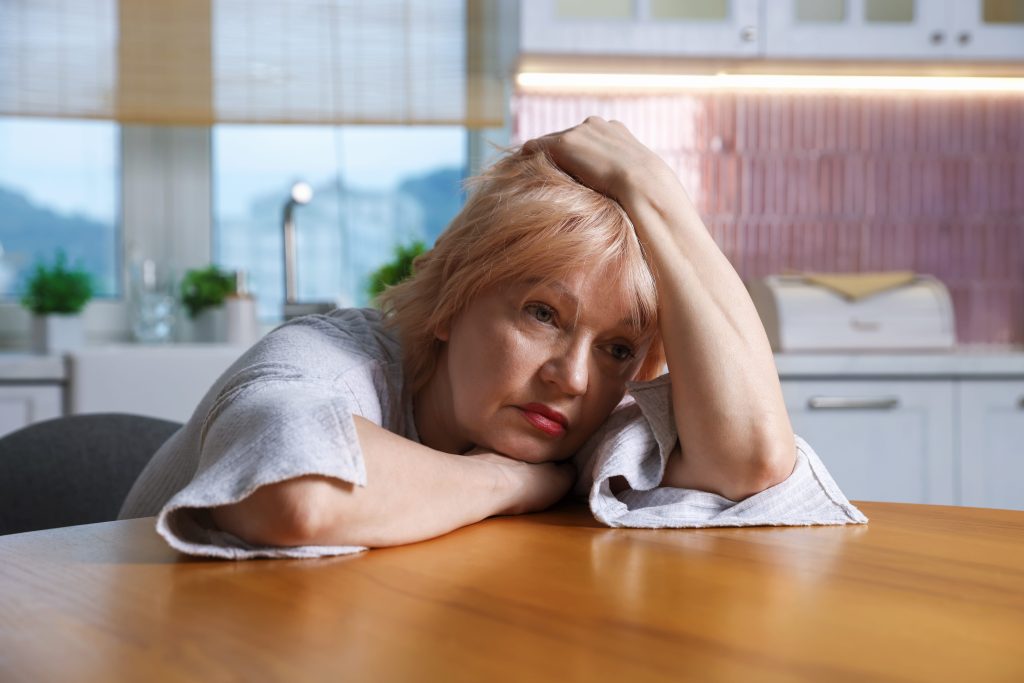 Midlife woman pausing mid-task in her kitchen, showing the brain fog of accumulated sleep debt