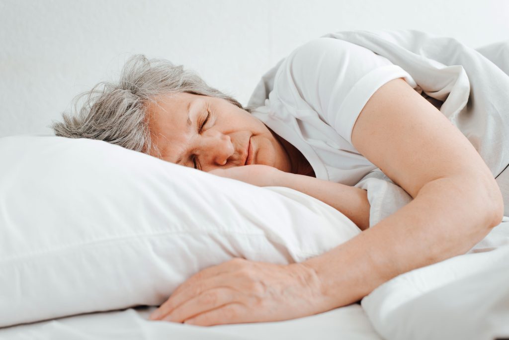 Midlife woman sleeping deeply in a dark bedroom, the rest estrogen and progesterone once supported