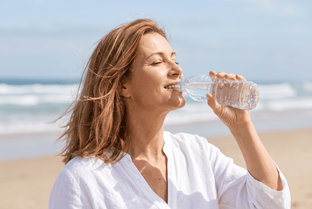 Woman drinking water at the beach, getting natural vitamin D from sunlight